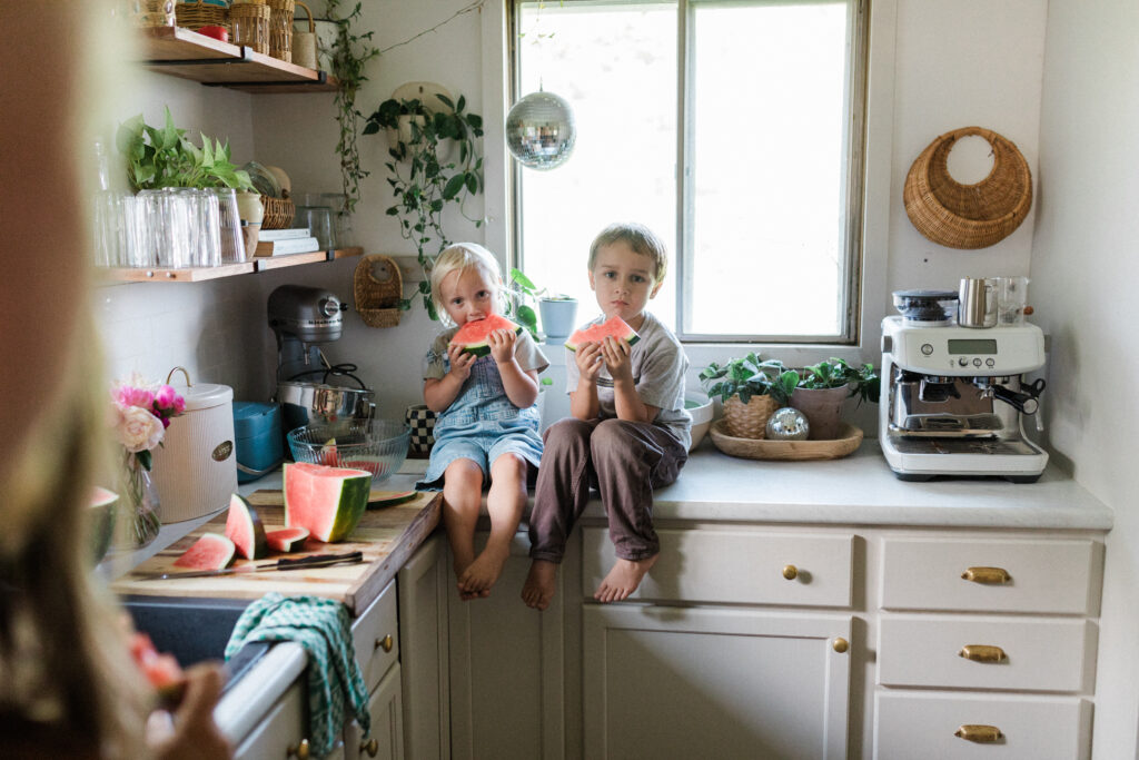 two children sitting on countertop eating slices of watermelon