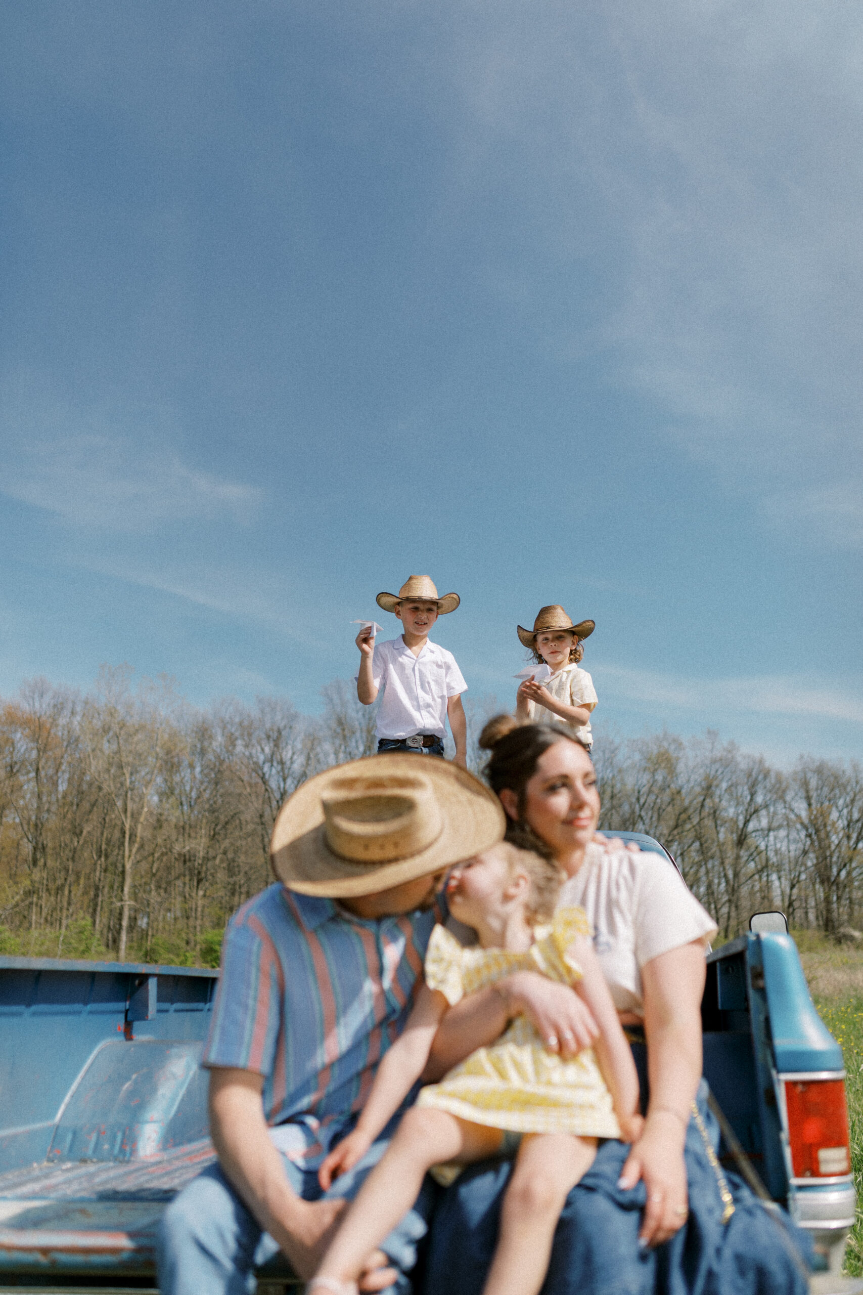 Family of five sitting on back of a pickup truck.